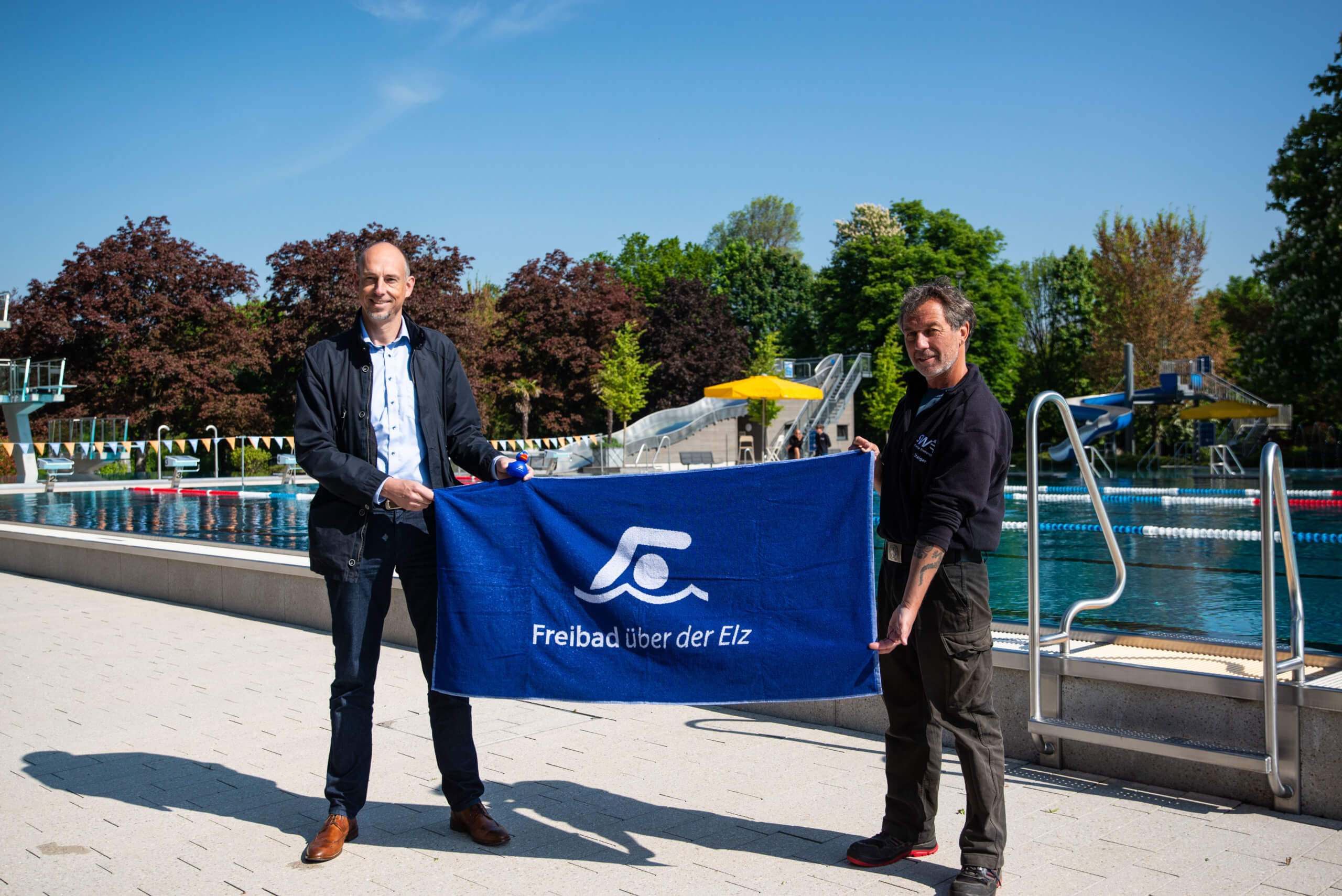 Stadtwerke Chef Björn Michel und Schwimmmeister Jörg Staiger präsentieren das neue Freibad Handtuch im Freibad über der Elz